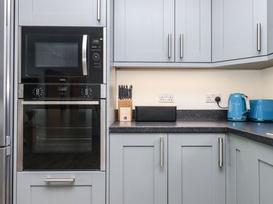 A kitchen with built-in microwave and oven a knife block black bread box blue kettle and toaster at Strawberry Bank - Nuthatch in Pyworthy near Bridgerule