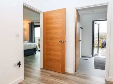 A hallway with wooden doors opening to a bedroom and an entrance area with a door leading outside at Strawberry Bank - Nuthatch in Pyworthy near Bridgerule