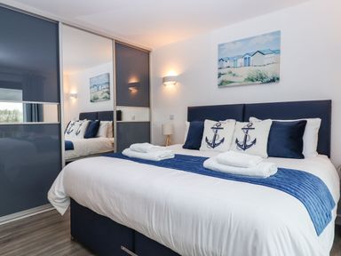 A bedroom with a double bed with white bedding and blue cushions and a painting on the wall at Strawberry Bank - Nuthatch in Pyworthy near Bridgerule