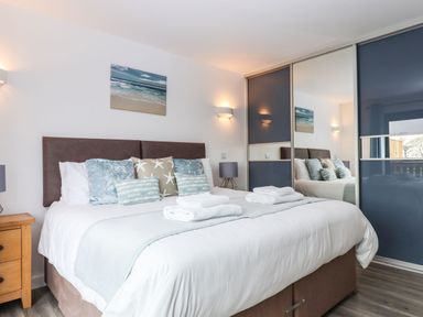 A bedroom with a double bed pillows and folded towels next to a wooden bedside table and mirrored sliding closets at Strawberry Bank - Nuthatch in Pyworthy near Bridgerule