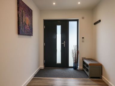 An entrance hallway with a black door a bench with storage and a framed painting on the wall at Strawberry Bank - Nuthatch in Pyworthy near Bridgerule