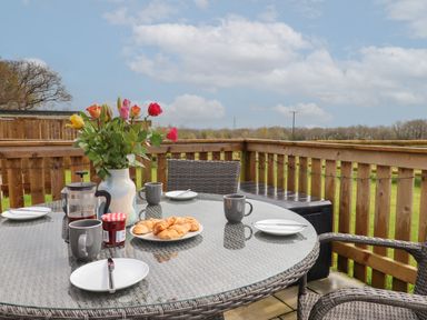 An outdoor patio table set with croissants coffee mugs a vase of flowers and a jar of jam at Strawberry Bank - Nuthatch in Pyworthy near Bridgerule