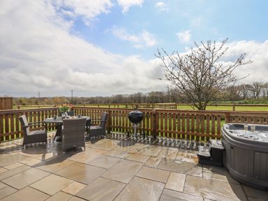An outdoor patio with a table and chairs a barbecue grill a hot tub and a tree behind a wooden fence at Strawberry Bank - Nuthatch Pyworthy near Bridgerule
