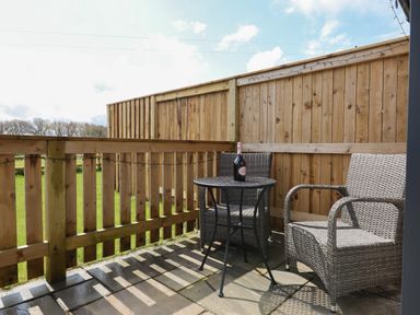 A small outdoor patio with two wicker chairs and a round table with a bottle on it at Strawberry Bank - Nuthatch in Pyworthy near Bridgerule