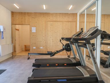 A gym room with two treadmills and a rowing machine with wood panel walls and mirrored wall at Strawberry Bank - Nuthatch in Pyworthy near Bridgerule