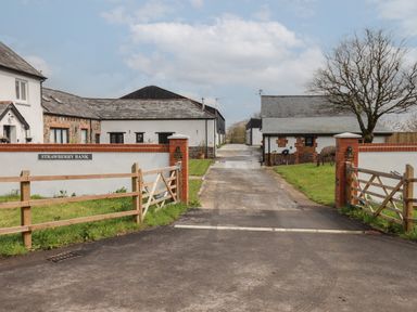 An entrance with wooden gates leading to white buildings with stone and brick details at Strawberry Bank in Pyworthy near Bridgerule