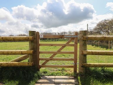 A wooden gate with a fence around a grassy field under a cloudy sky at Strawberry Bank - Nuthatch in Pyworthy near Bridgerule