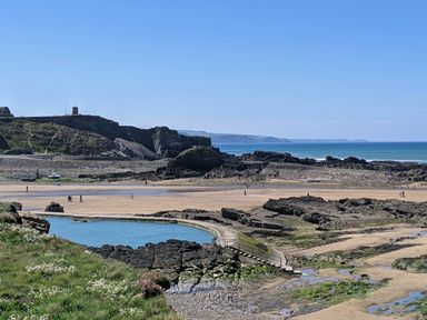 A rocky beach with people walking and a tidal pool near the shore at Strawberry Bank - Nuthatch in Pyworthy near Bridgerule