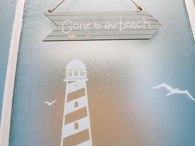 A frosted glass door with a lighthouse and seagulls design and a wooden sign hanging that says Gone to the beach at Riverdance Cottage in Lyme Regis