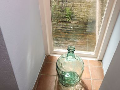 A glass bottle on a tiled floor near a window with a stone wall outside at Riverdance Cottage Lyme Regis