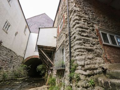 A narrow stone and brick building beside a shallow water stream under an archway in Lyme Regis