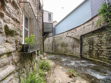 A narrow stream flowing between stone walls with a window and plants on the left side at Riverdance Cottage Lyme Regis