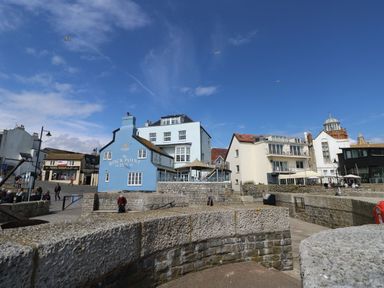 A stone pier and waterfront with buildings including The Rock Point Inn and people walking in Lyme Regis