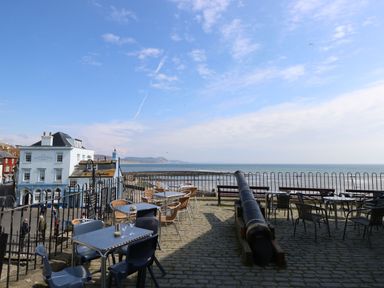 An outdoor seating area with tables, chairs, a cannon, and a view of the sea near The Rock Point Inn