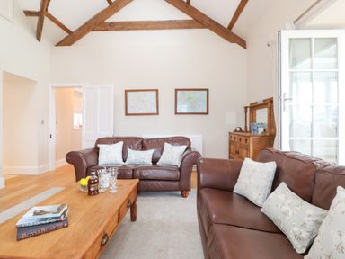 A living room with brown leather sofas and wooden coffee table under wooden ceiling beams at Farnelea West Fleetham near Seahouses