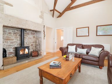 A living room with a stone fireplace a wood stove a brown leather sofa a wooden coffee table and framed maps on the wall at Farnelea West Fleetham near Seahouses