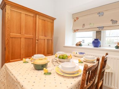 A dining table with bowls plates and fruit in front of a wooden cupboard and window at Farnelea in West Fleetham near Seahouses