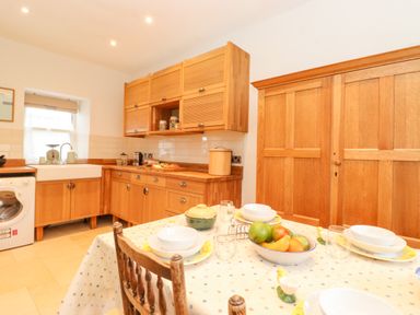 A kitchen with wooden cabinets a dining table set with bowls glasses and a fruit bowl at Farnelea in West Fleetham near Seahouses