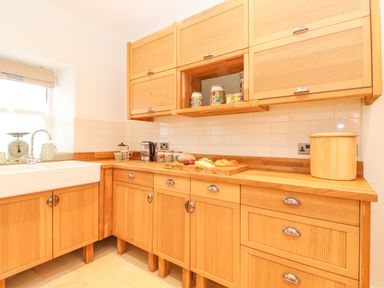 A kitchen with wooden cabinets a white sink a kettle jars and food on the counter at Farnelea West Fleetham near Seahouses