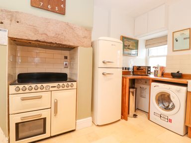 A kitchen with a cream stove under a stone hood a cream refrigerator a washing machine and a microwave on a wooden countertop at Farnelea West Fleetham near Seahouses