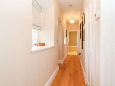 A narrow hallway with wooden floor leading to a bathroom with tiled walls at Farnelea in West Fleetham near Seahouses