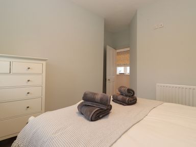 A bedroom with a bed with towels on it and a white chest of drawers near an open door at Farnelea in West Fleetham near Seahouses