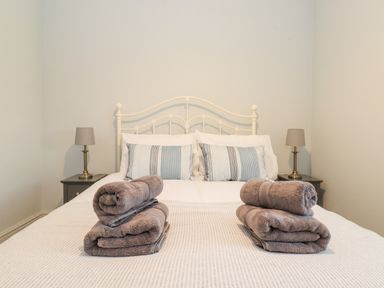 A bedroom with a white metal bedframe, two striped pillows, bedside tables with lamps and folded towels on the bed at Farnelea West Fleetham near Seahouses