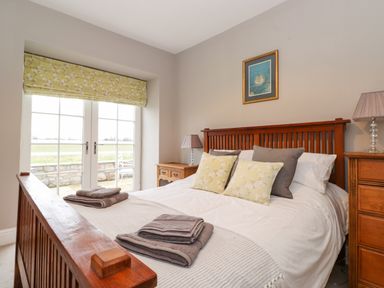 A bedroom with a wooden bed frame bedside tables lamps and a window with floral blinds at Farnelea West Fleetham near Seahouses