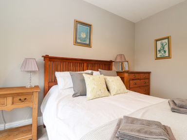 A bedroom with a wooden bed frame side table lamps and framed pictures at Farnelea in West Fleetham near Seahouses