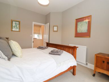 A bedroom with a wooden bed frame pillows and towels with wall art and a wooden cabinet at Farnelea West Fleetham near Seahouses