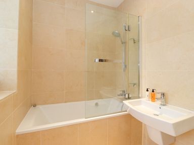 A bathroom with a bathtub shower combination and a wall-mounted sink at Farnelea West Fleetham near Seahouses