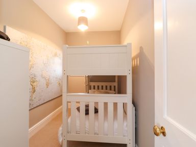 A small bedroom with a white bunk bed a map on the wall and a white wardrobe at Farnelea West Fleetham near Seahouses