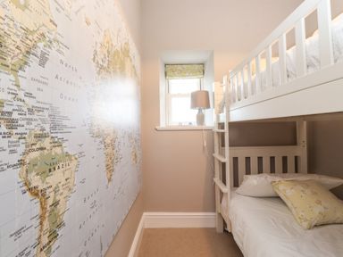 A bedroom with white bunk beds a lamp on the window sill and a world map wall at Farnelea West Fleetham near Seahouses