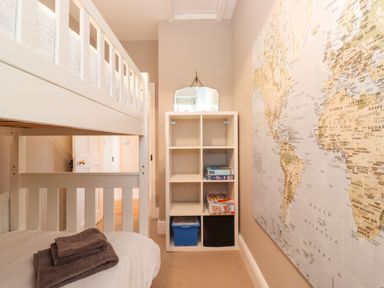 A bedroom with a white bunk bed towels on the bottom bed a white shelving unit with board games and a large world map on the wall at Farnelea West Fleetham near Seahouses