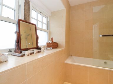 A bathroom with a bathtub glass shower screen and a window ledge with a mirror basket and toiletries at Farnelea West Fleetham near Seahouses