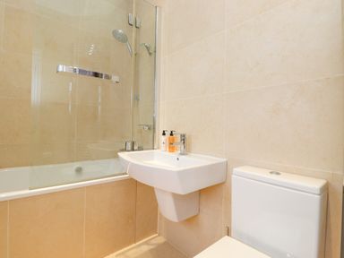 A bathroom with a bathtub glass shower screen pedestal sink with soap bottles and a toilet at Farnelea in West Fleetham near Seahouses