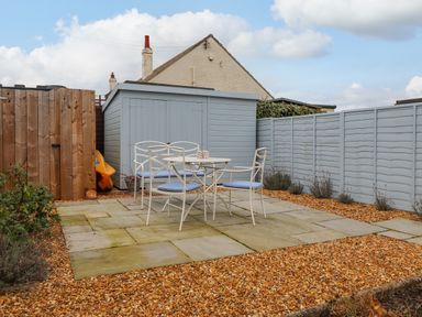 An outdoor patio area with a table and chairs surrounded by gravel and fences at Farnelea in West Fleetham near Seahouses