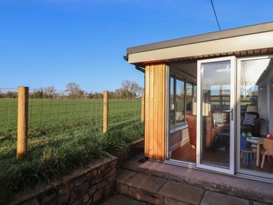 A glass door opening to a room with chairs and a table next to a grassy field with a wire fence at Farnelea in West Fleetham near Seahouses