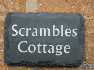 A dark stone plaque with Scrambles Cottage written on it mounted on a stone wall at Scrambles Cottage in Stoke-Sub-Hamdon Somerset