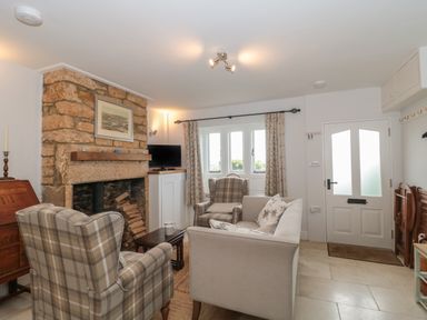 A living room with stone fireplace plaid armchairs sofa and a television at Scrambles Cottage in Stoke-Sub-Hamdon Somerset