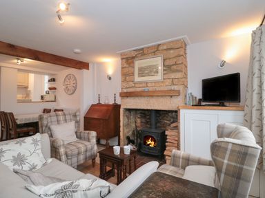 A living room with a stone fireplace and wood stove surrounded by armchairs and a sofa at Scrambles Cottage in Stoke-Sub-Hamdon Somerset