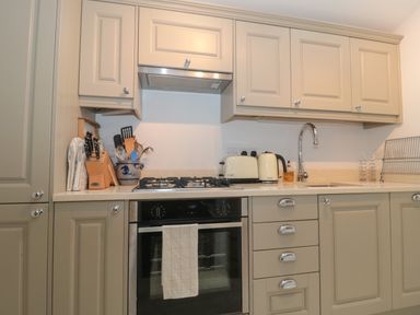 A kitchen with beige cabinets a gas stove an oven a sink utensils and appliances at Scrambles Cottage in Stoke-Sub-Hamdon Somerset