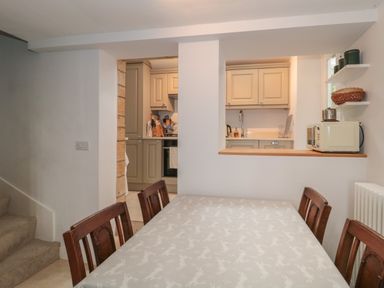 A dining area with wooden chairs and a table facing a kitchen with beige cabinets at Scrambles Cottage in Stoke-Sub-Hamdon Somerset
