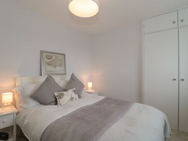 A bedroom with a bed and pillows between bedside tables with lamps and a framed picture above the headboard at Scrambles Cottage in Stoke-Sub-Hamdon Somerset