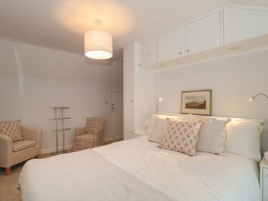 A bedroom with a double bed and pillows two armchairs a standing rack and wall cabinets at Scrambles Cottage in Stoke-Sub-Hamdon Somerset