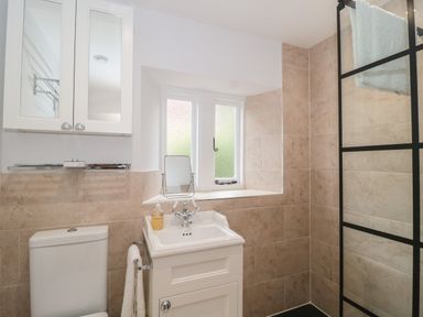 A bathroom with a toilet, white sink with cabinet, towel rack, frosted window, and a glass shower screen with black frame at Scrambles Cottage in Stoke-Sub-Hamdon Somerset