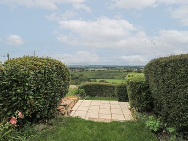 A garden with trimmed hedges and a paved patio overlooking fields and hills at Scrambles Cottage in Stoke-Sub-Hamdon Somerset