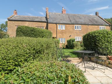 A garden with a patio table and chairs in front of a stone house at Scrambles Cottage in Stoke-Sub-Hamdon Somerset