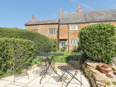 A patio with metal table and chairs and trimmed hedges in front of a stone house at Scrambles Cottage in Stoke-Sub-Hamdon Somerset