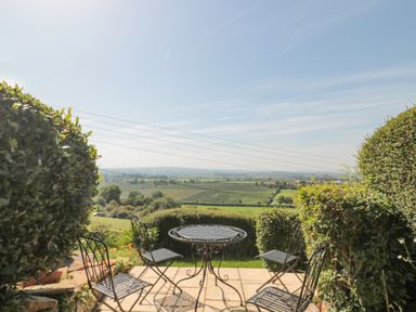 A patio with a metal table and four chairs overlooking fields and greenery at Scrambles Cottage in Stoke-Sub-Hamdon Somerset
